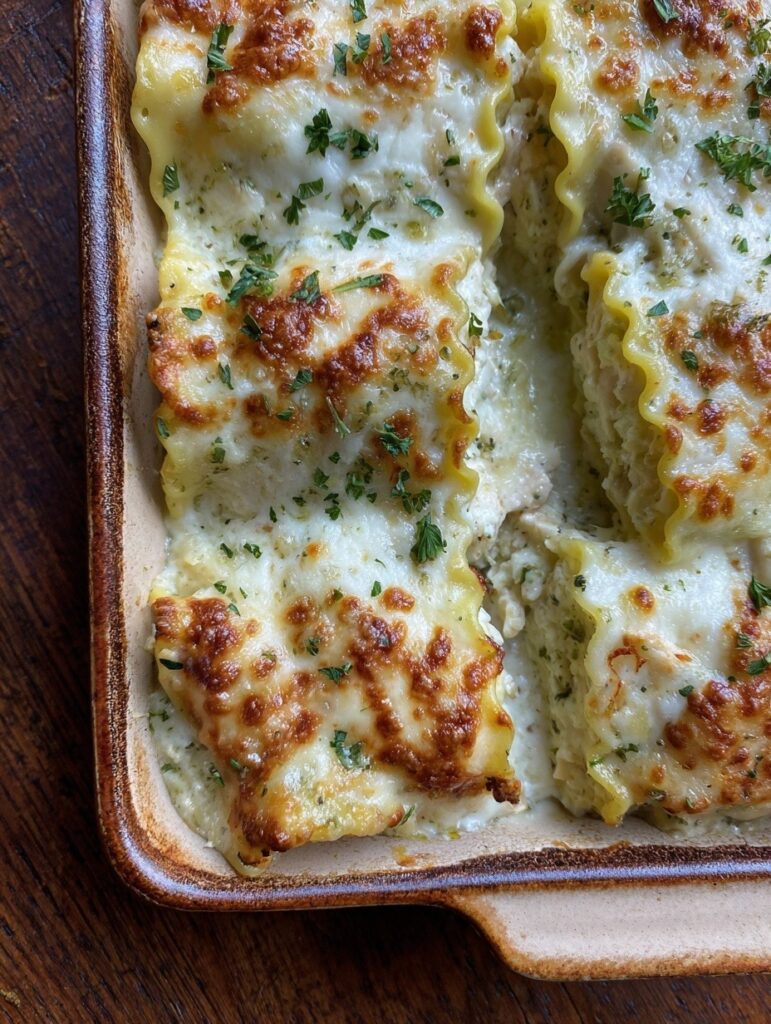 Cheesy chicken Alfredo lasagna rolls with melted mozzarella and Alfredo sauce bubbling in baking dish, lightly browned on edges and topped with fresh parsley.