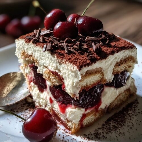 Slice of cherry amaretto tiramisu showing layers of mascarpone cream with fresh cherries between ladyfinger cookies, dusted with cocoa powder