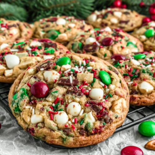 Golden Christmas kitchen sink cookies loaded with M&Ms, white chocolate chips, pretzels, and sprinkles on holiday background