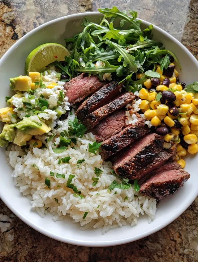Overhead view of homemade Tex-Mex steak bowl with sliced steak, cilantro lime rice, and corn avocado salsa in white bowl