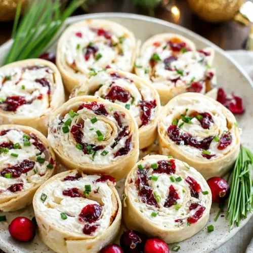 Festive Christmas cranberry roll-ups with cream cheese and feta on white platter showing red cranberries and green chives - easy holiday appetizer