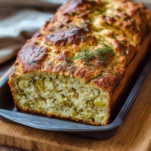 Sliced golden dill pickle bread on wooden cutting board showing soft fluffy texture with visible pickle pieces throughout the crumb