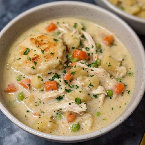 Healthy chicken pot pie soup in white bowl with carrots, potatoes, and chicken in creamy broth with black pepper on gray background
