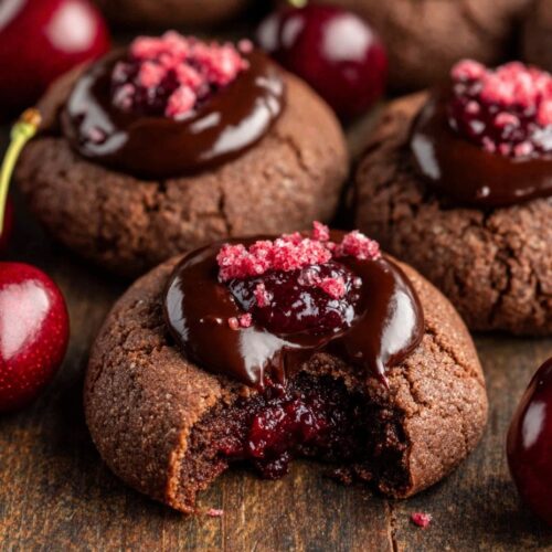 Fudgy chocolate cherry thumbprint cookies filled with chocolate ganache on wooden board with fresh cherries - valentine dessert recipe
