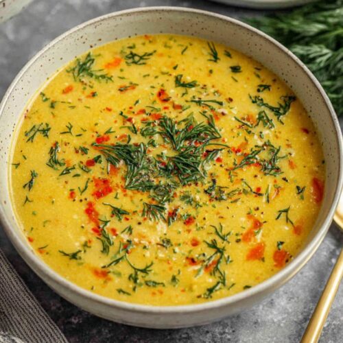 Creamy carrot potato soup in ceramic bowl garnished with fresh parsley, showing orange broth with visible vegetable chunks, served with crusty bread on kitchen counter